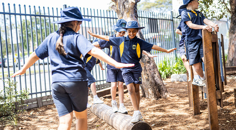 Students balancing on a log in the playground at St Mary's Primary School Rydalmere