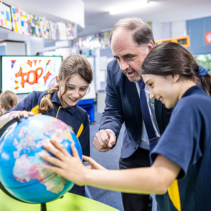 Principal Richard Blissenden looking at a globe with studets in the classroom at St Mary's Primary School Rydalmere
