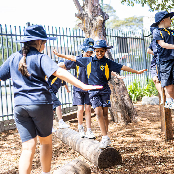 Student balancing on a log in the playground at Students learning together in the classroom with their teacher at St Mary's Primary School Rydalmere